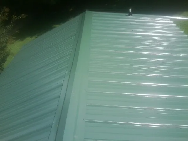New green metal panels meeting at the ridge of a roof — Flat Roof Repair work by our crew in Lancaster