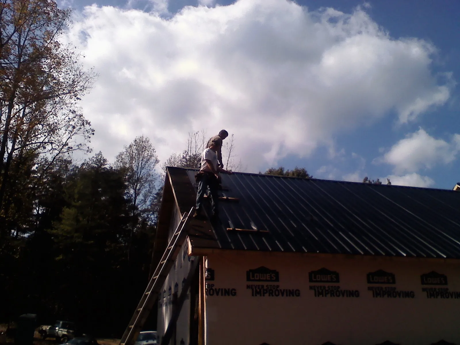 Roofer fastening dark metal panels high against a cloudy sky, from a Roof Inspection job in Lancaster